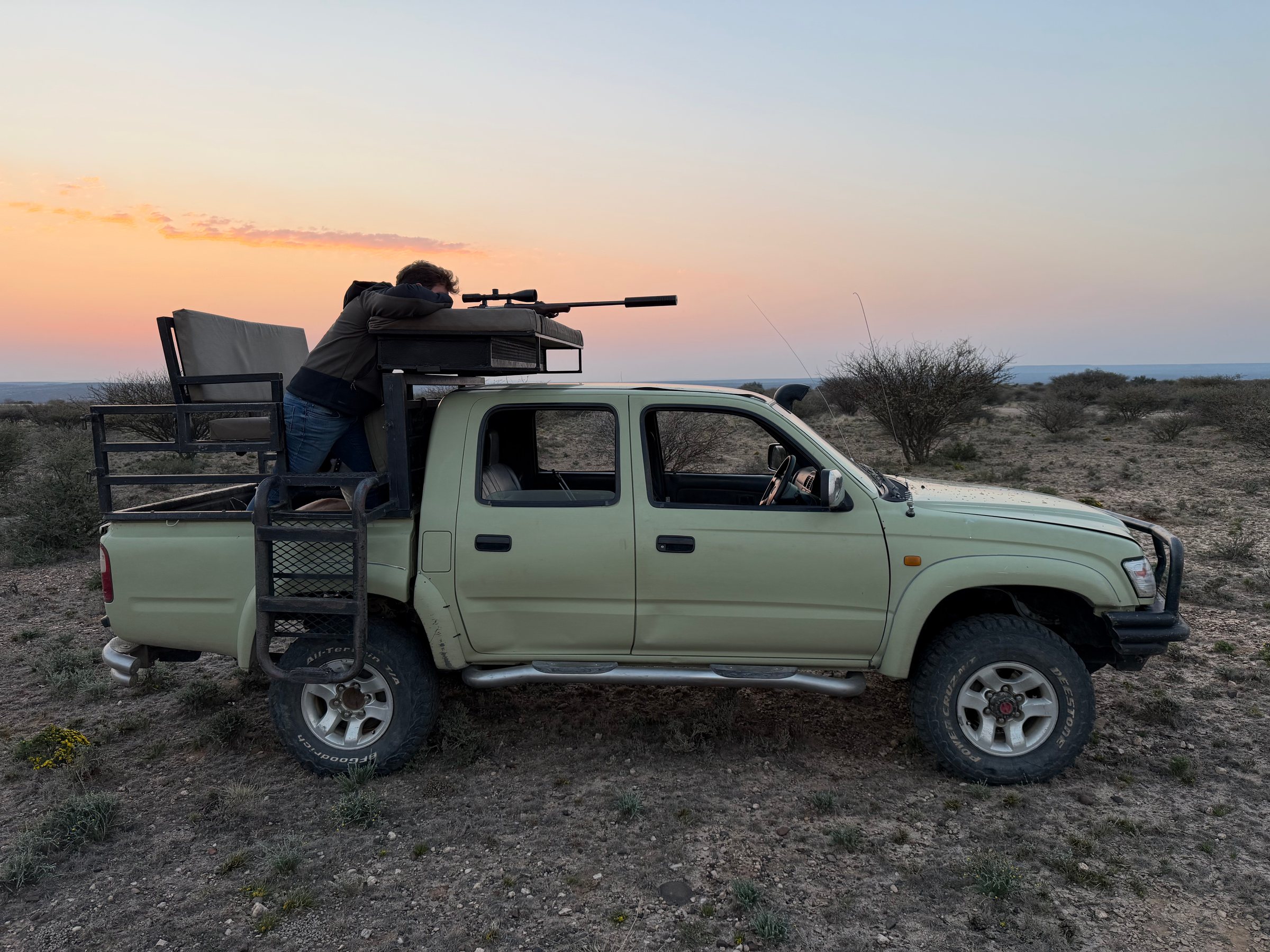 A hunter rests his rifle on the hunting vehicle at dusk