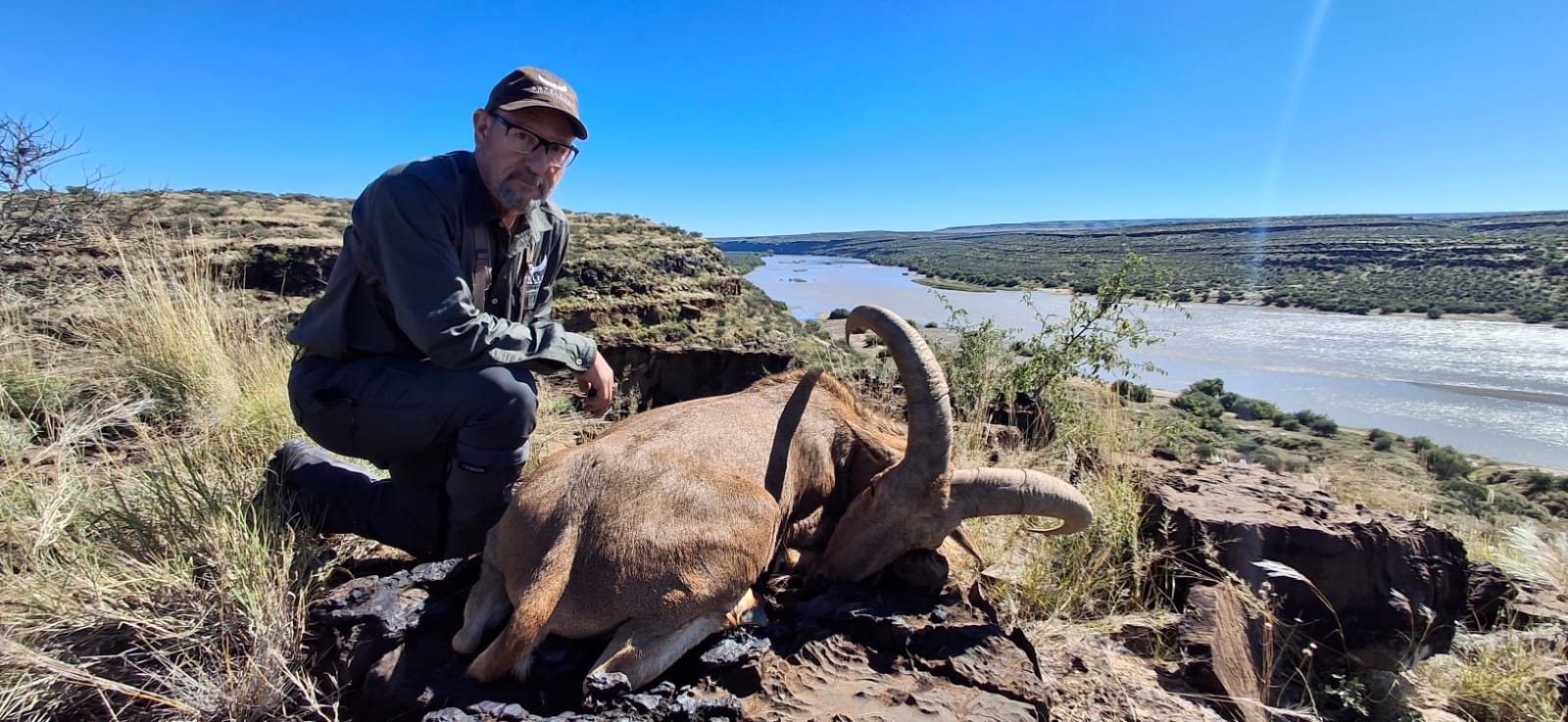 A hunter with a Barbary sheep on the cliffs above the river