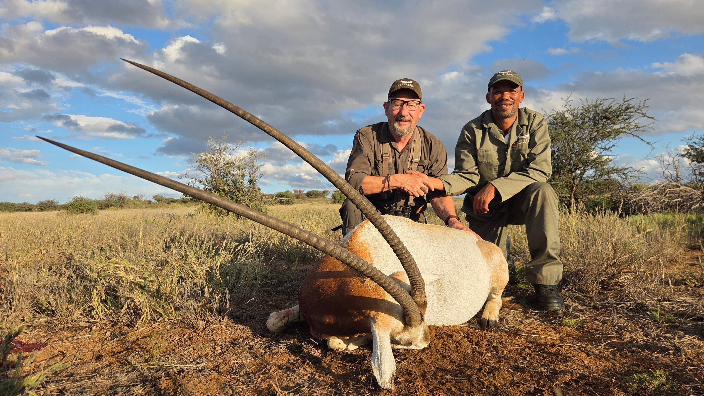 A hunter and his tracker with a scimitar oryx under a big sky