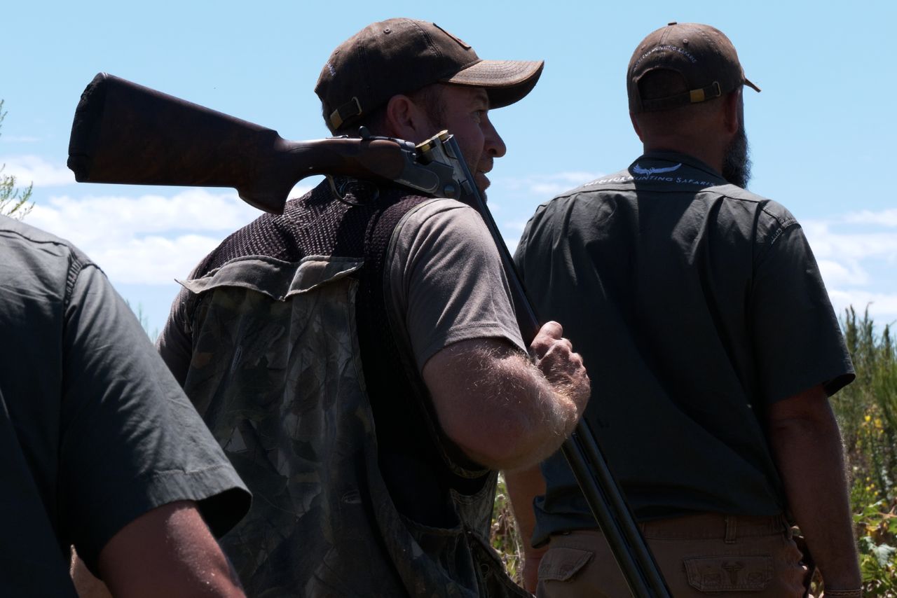 Bateleur hunters walk out with a rifle under a clear sky