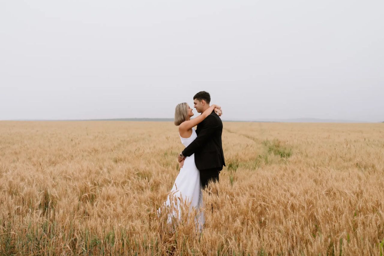 A bride and groom embrace in a golden field